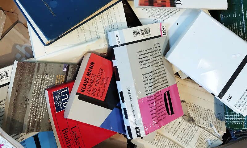 Bücher verschiedener Größen und Farben aus Papier liegen durcheinander. Mit Karton- oder Pappe-Einband. Manche sind offen. Sie wurden vom Kaufhaus entsorgt. Verpackung einer Heckenschere aus Wellpappe aus einem Supermarkt.