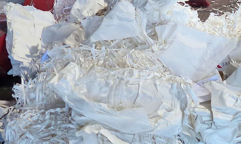 Altpapier aus Druckresten, Druckausschuss liegt vor der Papier-Presse in der Halle vom Papier-Recyclingbetrieb Xpress Paper. Weißer Druckverschnitt wurde von einer Druckerei entsorgt und wird nun zu Papierballen gepresst und recycelt.
