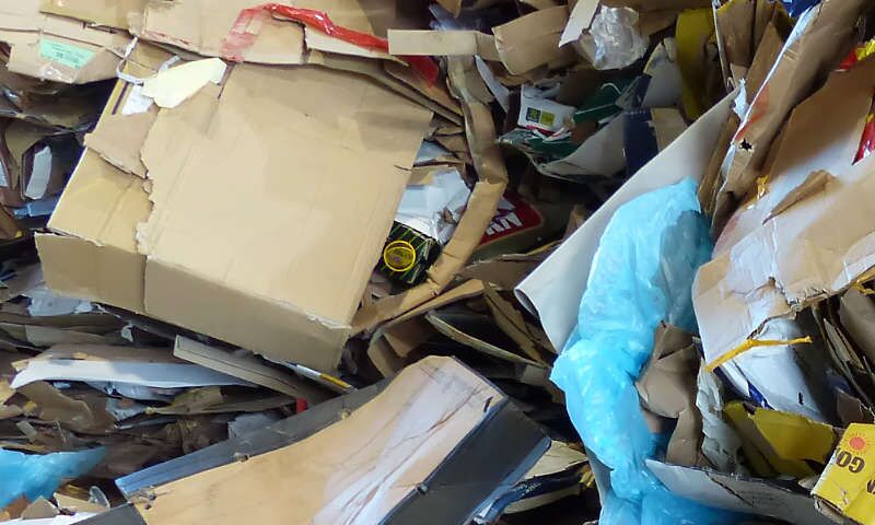 Pappe-Ausschussware aus einem Wellpappenwerk in einem ungeordneten Haufen von Kartons aus Wellpappe. Dazwischen haben sich einige bunte Verpackungen aus einem Supermarkt versteckt. Der Papierabfall wird sortiert und weiterverarbeitet.