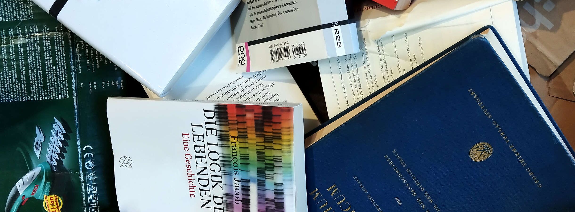 Ein kaputter beiger Karton. Darüber liegen mehrere entsorgte Bücher aus dem Einzelhandel. Eine dunkelgrüne Kartonverpackung von einer Bosch-Heckenschere mit CE-Zeichen. Dieser Papier- und Kartonmüll wird beim Entsorgungsunternehmen recycelt.