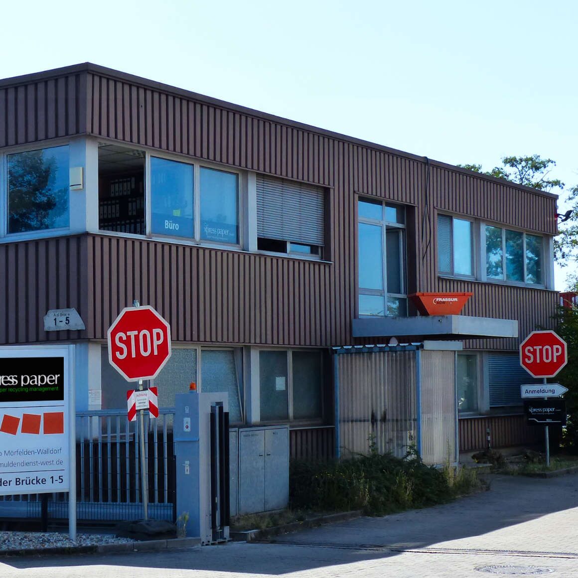 Terrakotta Bürogebäude bei der Einfahrt zum seit 2012 agierenden und zertifizierten Dienstleisters für ganzheitliche Entsorgungskonzepte, effiziente Altpapier, Pappe-Verwertung und Handel mit Recycling-Rohstoffen. Rote Stop-Schilder, aufgeräumtes Gelände.