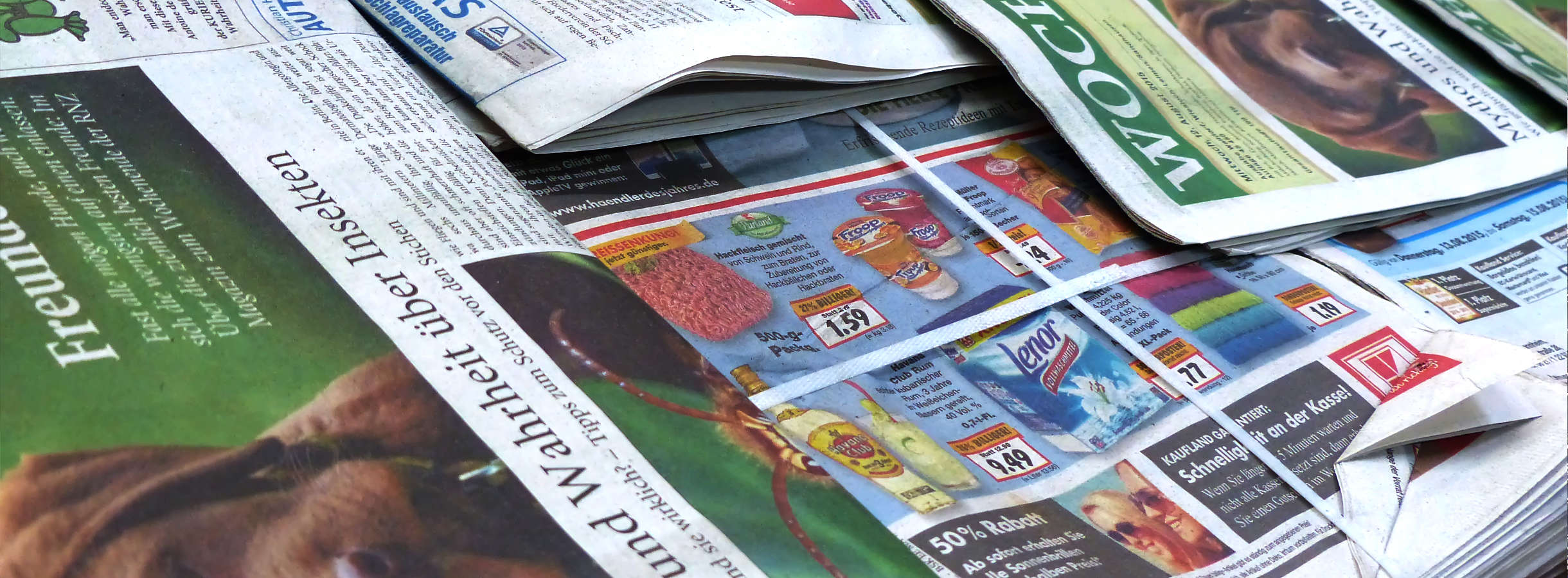 Überschuss und Reste bunter Lokal- und Werbe-Zeitungen verschiedener Verlage, zusammengebunden und auf Palette gestapelt, warten auf Ihre Weiterverarbeitung. Das Altpapier wurde von Verlagen gesammelt, entsorgt und wird zu Papierballen gepresst.