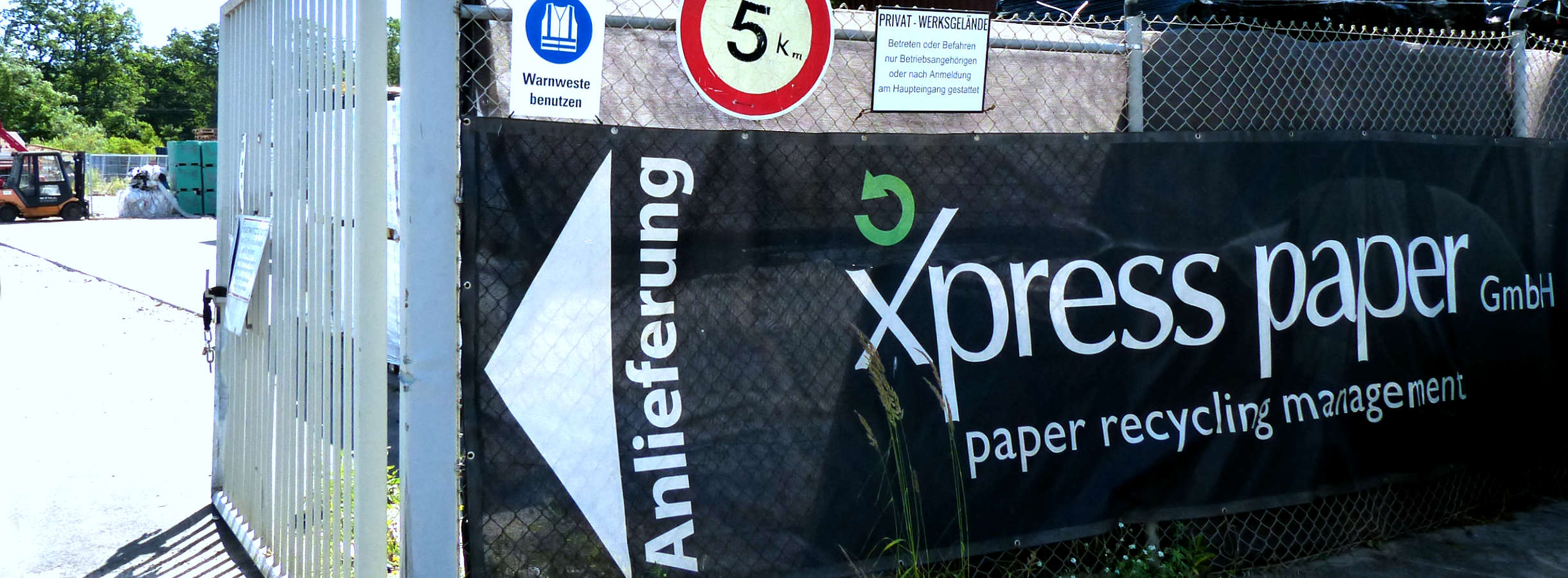 Zufahrt zur Anlieferung und LKW-Waage entsorgter Recycling-Rohstoffe. Großes Tor ist offen und Gewährt einen Blick auf das Gelände des Entsorgungsbetriebs für Frankfurt-Rhein-Main in Mörfelden-Walldorf. Am Zaun ist das Logo mit Einfahrtsschild angebracht.