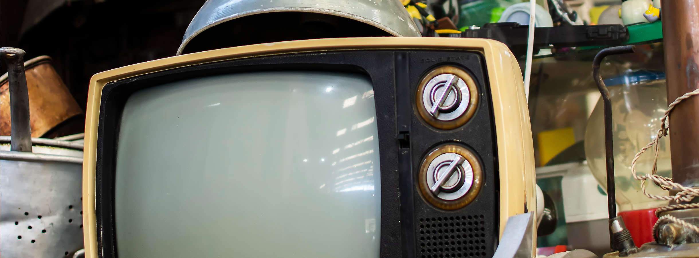 E-Schrott auf den Lagerplätzen im Hamburger Recyclingunternehmen. Ein kleines Fernsehgerät mit einer alten Fernsehröhre. Neben dem Bildschirm sind zwei drehbare Elektroschalter angebracht, darunter ein Lautsprecher. Auf dem Elektrogerät liegt eine Lampe.