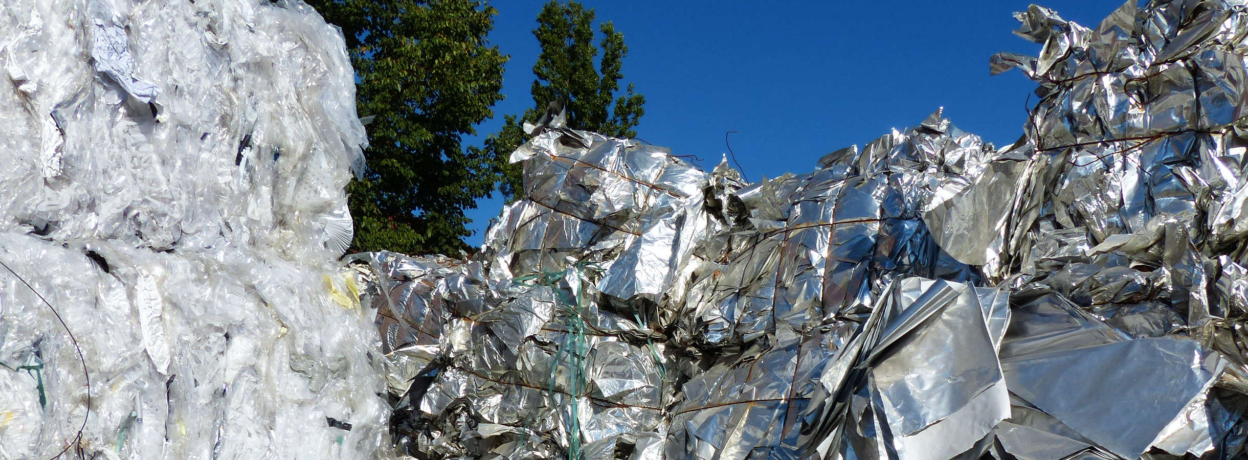 Gepresste Ballen aus sortiertem Kunststoffabfall und Plastikabfall liegen gestapelt auf dem Werksgelände des Recyclings-Unternehmens Xpress Paper in Mörfelden-Walldorf. Ein Stapel aus transparentem Plastik und drei aus silbernem Kunststoff.