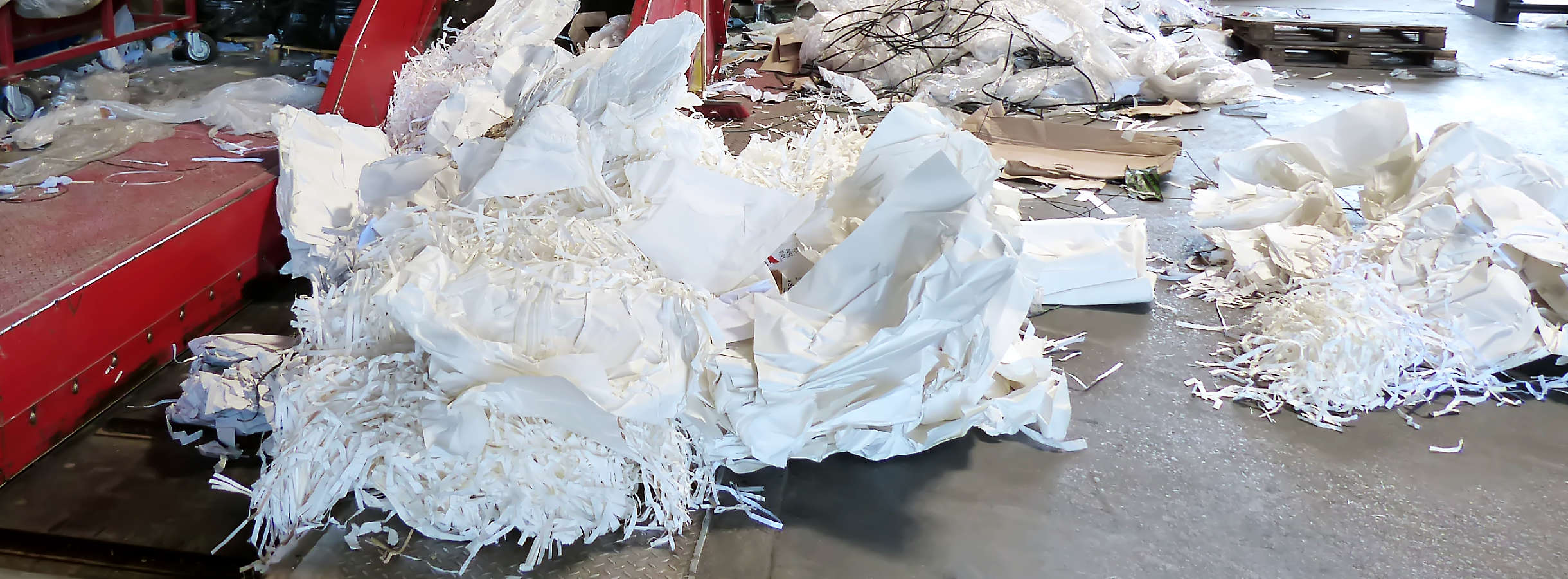 Mehrere Haufen aus Altpapier & Plastik liegen unordentlich auf dem Boden. Sie wurden nach einer Reklamation zu Sorten sortiert. Sauberer Abfall erzielt höhere Preise. Nun können diese Rohstoffe recycelt und erneut dem Rohstoffkreislauf hinzugefügt werden.